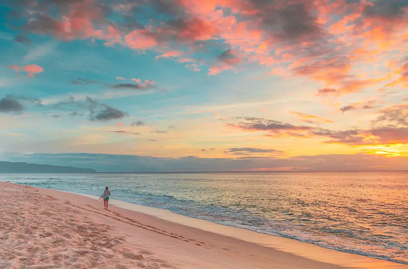Individual strolling on a secluded beach with a breathtaking pink and blue sunset in the background