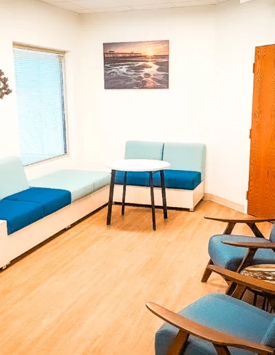 Landscape image of Dovetail Orthopedics waiting room with wall art, benches with blue cushions and 2 blue armchairs with side table
