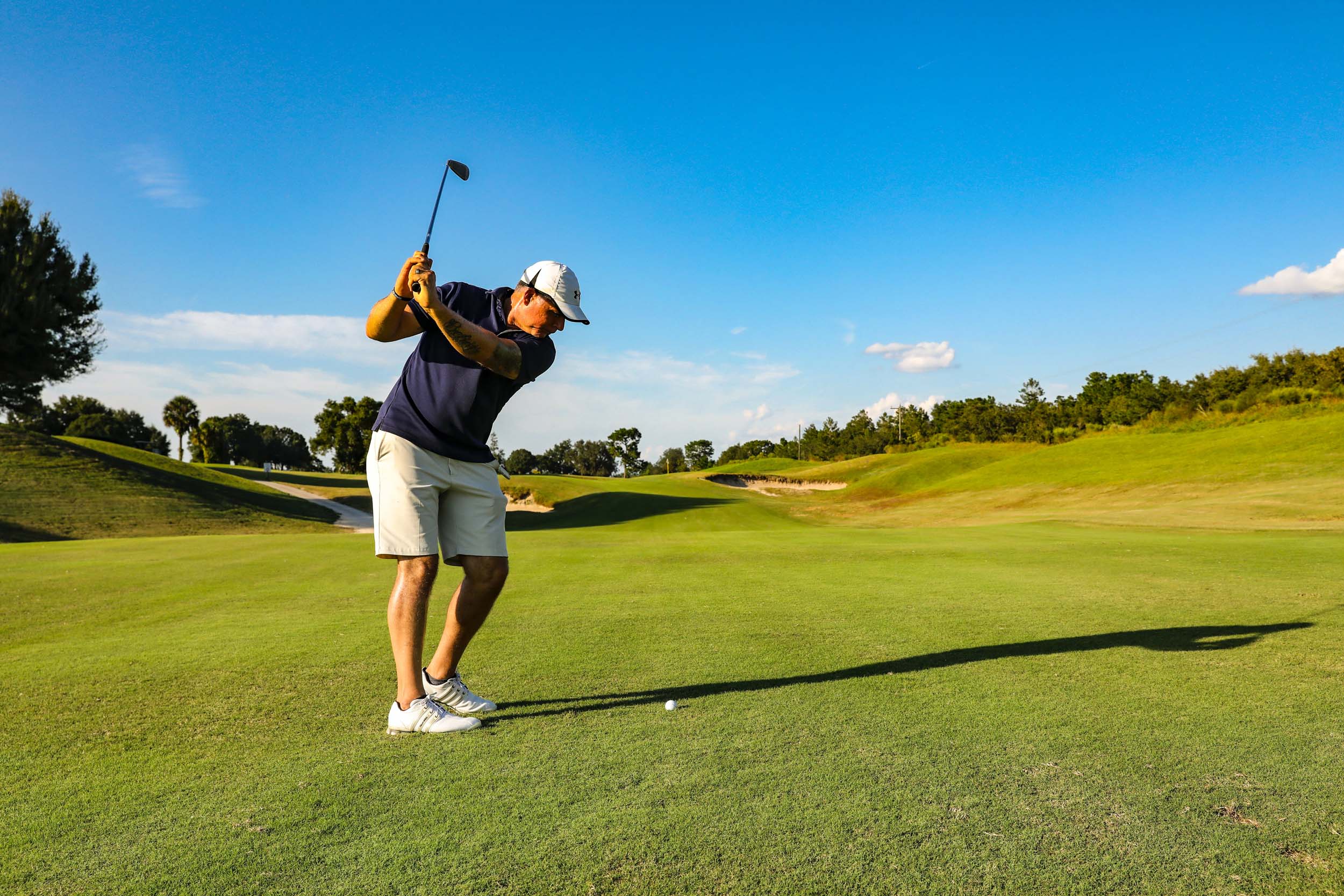 Man swinging golf club on golf course with blue sky